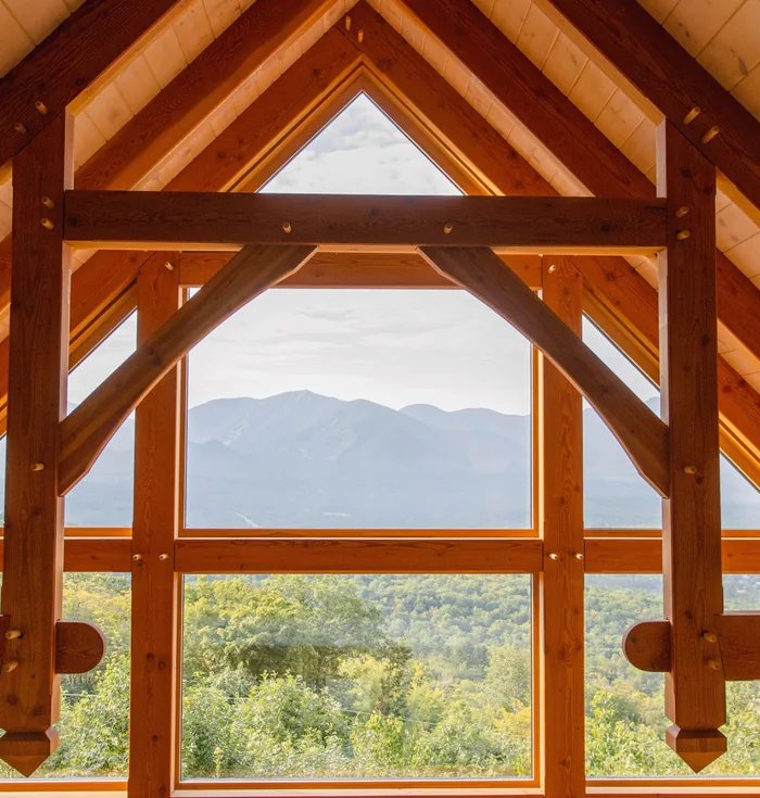 Timber trusses and a tall gable window in a new house, looking out over wooded hills to a mountain ridge