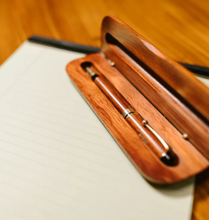 A wooden pen case and pen resting on a yellow legal pad on a wooden desk